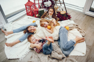 A family posed on the floor with fall and winter decorations around them. The weather outside the window is cold, but the mother and a child have bare feet in a home likely warmed by an electric furnace or a natural gas furnace.