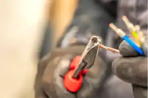 A Perfect Plumbing, Heating & Air technician in gloves trims a copper electrical wire with wire cutters during a service call.