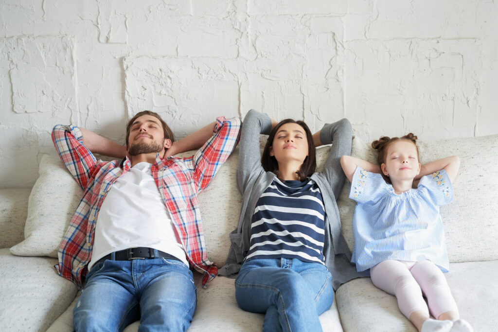 A family relaxes on a sofa with hands behind their heads, enjoying comfort provided by Perfect Plumbing, Heating & Air’s services.